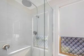 A modern bathroom with a glass-enclosed shower, a bathtub, and a window with a patterned view. - Reflections Holiday Park Ferry Reserve (Brunswick Heads)