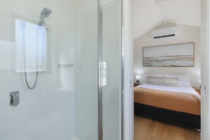 A hotel room with a glass door leading to a shower area, a bed with a headboard, and a painting on the wall. - Reflections Holiday Park Ferry Reserve (Brunswick Heads)