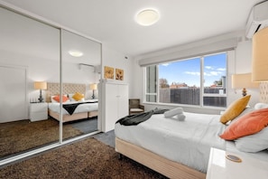 A modern bedroom with a large bed, a mirror, and a view of the outside. - Staycentral - Brunswick Vibe Parkville (Melbourne)