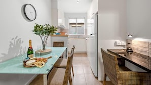 A compact kitchen with a dining area, a clock on the wall, and a window providing natural light. - Staycentral - Brunswick Vibe Parkville (Melbourne)