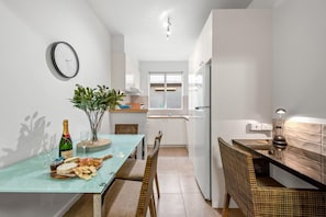 A compact kitchen with a dining area, a clock on the wall, and a window providing natural light. - Staycentral - Brunswick Vibe Parkville (Melbourne)