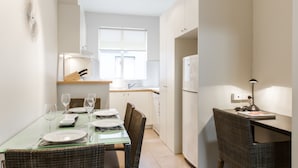 A compact kitchen with a dining area, a refrigerator, and a table set for two with glasses and plates. - Staycentral - Brunswick Vibe Parkville (Melbourne)