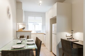 A compact kitchen with a dining area, a refrigerator, and a table set for two with glasses and plates. - Staycentral - Brunswick Vibe Parkville (Melbourne)
