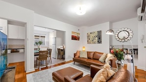 A modern living room with a brown leather sofa, a coffee table, and a dining area with chairs. - Staycentral - Brunswick Vibe Parkville (Melbourne)