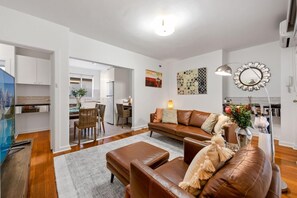 A modern living room with a brown leather sofa, a coffee table, and a dining area with chairs. - Staycentral - Brunswick Vibe Parkville (Melbourne)