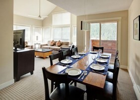 Un comedor con una mesa larga dispuesta para cuatro personas, un sofá y un televisor al fondo.