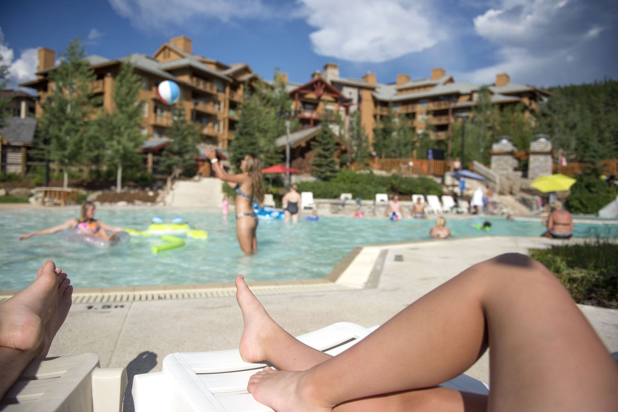 A pool area with lounge chairs, a person relaxing, and a building with multiple balconies in the background.