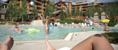 Une zone avec une piscine, des chaises longues, une personne se relaxant et, en arrière-plan, un bâtiment doté de nombreux balcons.