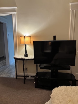 A living room with a flat-screen TV on a stand, a lamp on a side table, and a fluffy white rug.