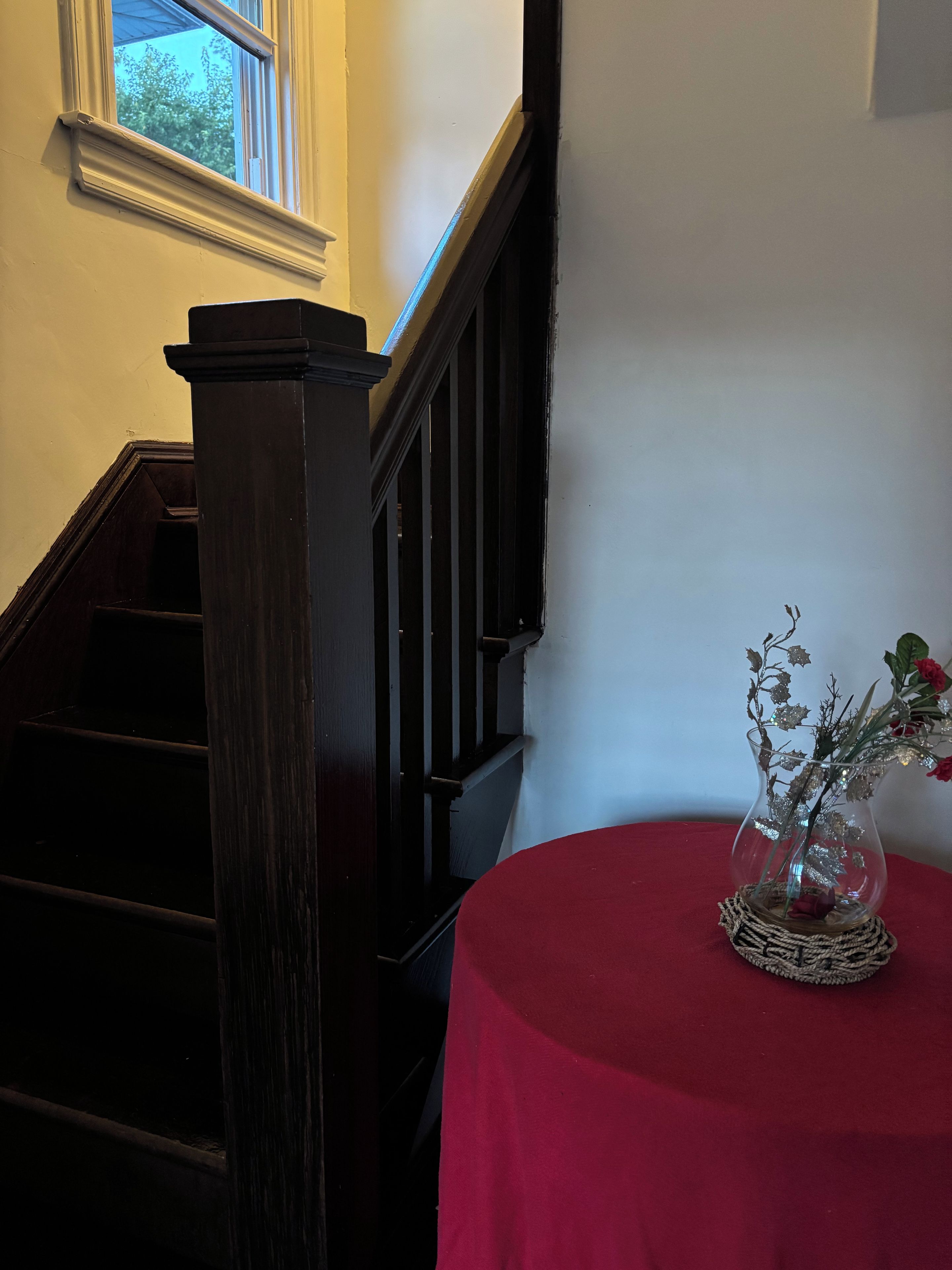 Een trap met een donker houten leuning en een rode tafel met een glazen vaas met bloemen.