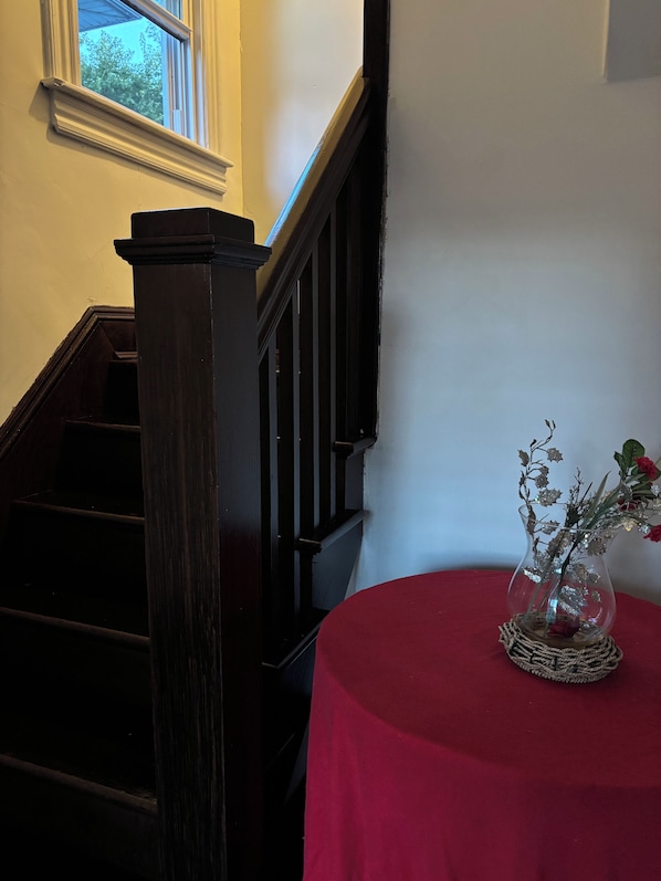 A staircase with a dark wooden handrail and a red table with a glass vase containing flowers.
