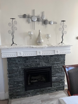 A fireplace with a white mantel, a stone surround, and decorative mirrors and glassware.