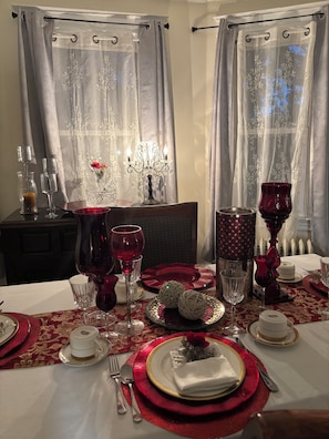 A dining table set with red and gold tableware, a chandelier, and curtains.