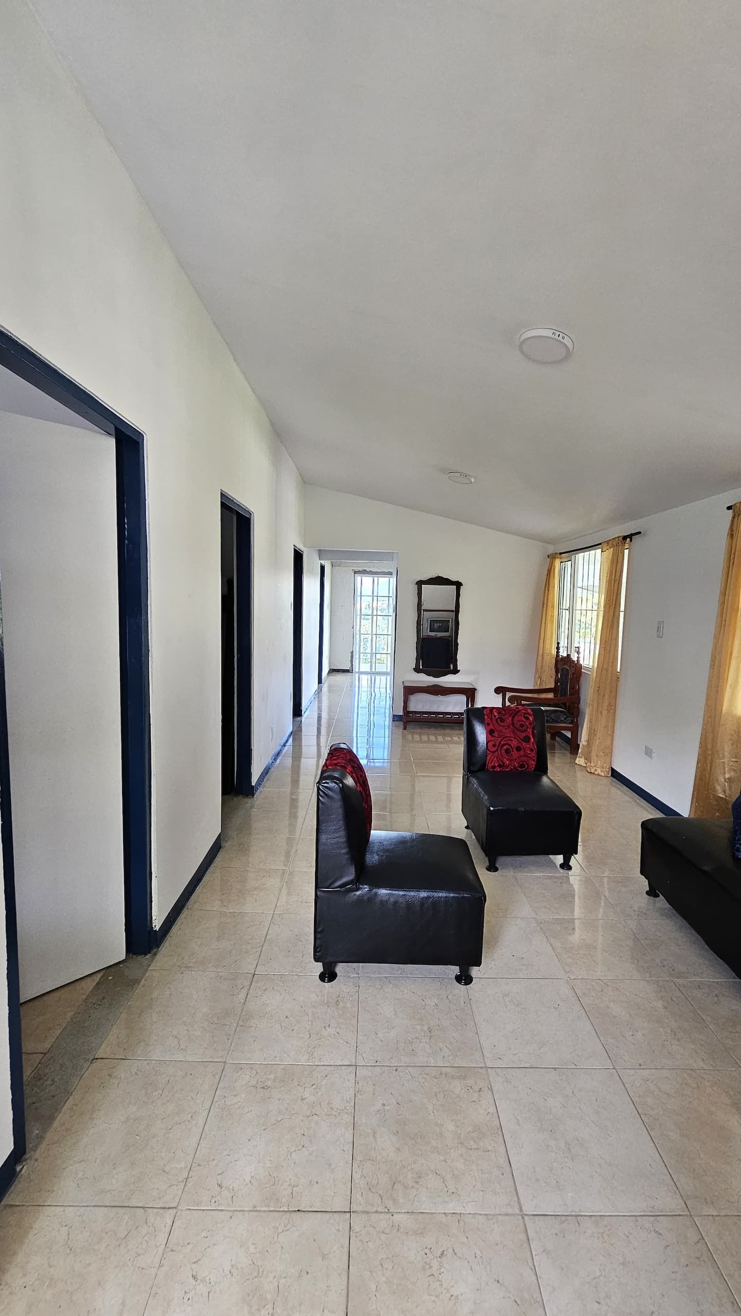 Amplia sala de estar con televisor grande, dos sofás de cuero negro y piso de baldosas.