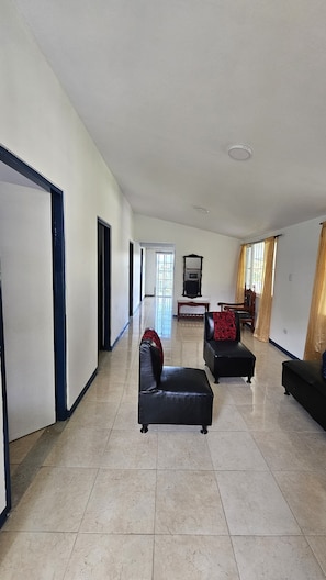 A spacious living room with a large television, two black leather sofas, and a tiled floor.