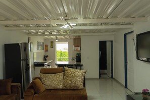A living room with a sofa, a television, and a kitchen in the background. - Whole farmhouse near Pereira: private pool, BBQ, soccer field, sleeps 30 (Arabia)