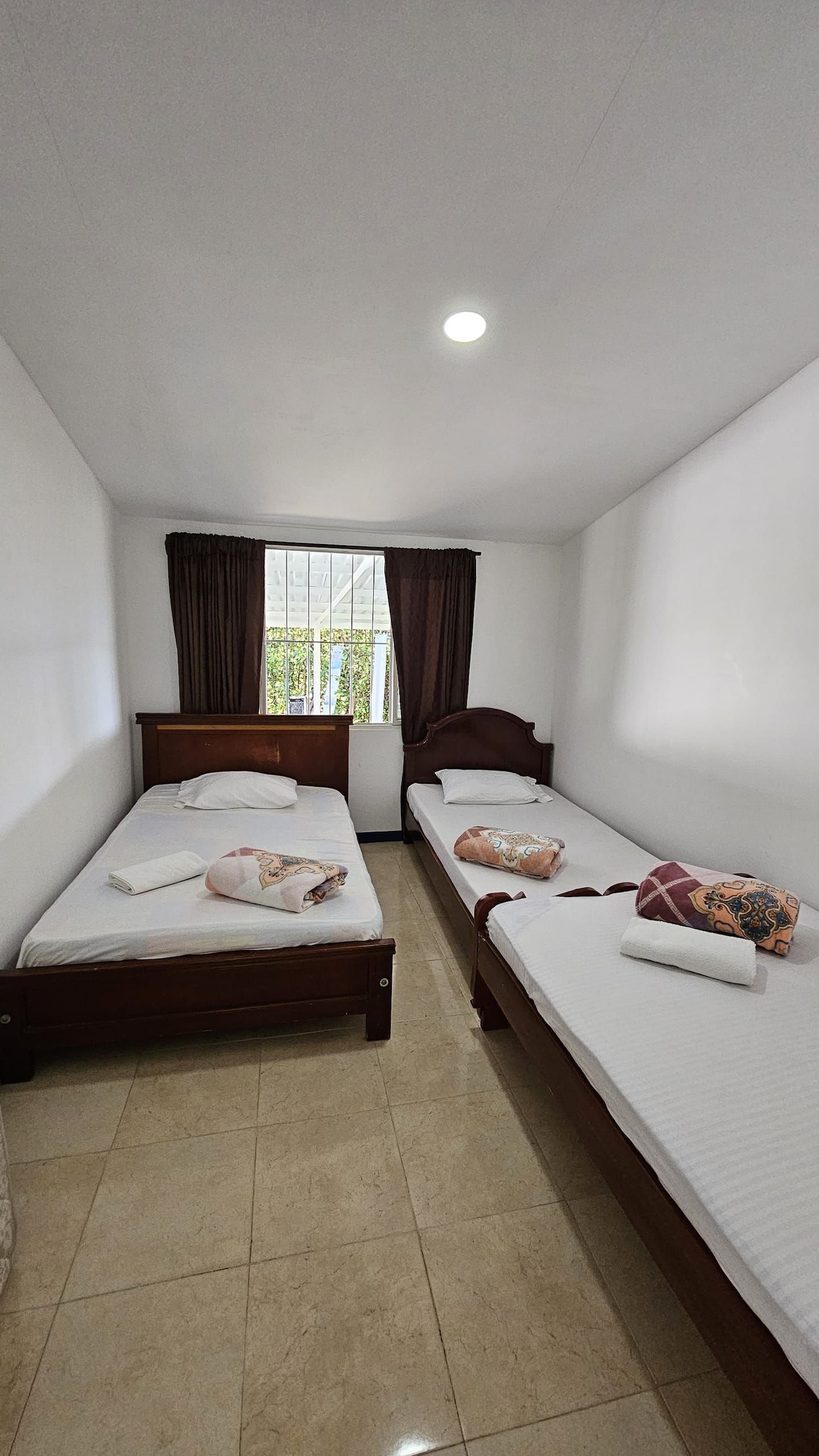 A room with two single beds, a window with curtains, and a ceiling light.