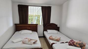 A room with two single beds, a window with curtains, and a ceiling light.