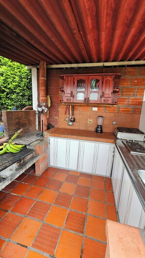 An outdoor kitchen with a brick wall, a wooden cabinet, and a gas stove. - Whole farmhouse near Pereira: private pool, BBQ, soccer field, sleeps 30 (Arabia)