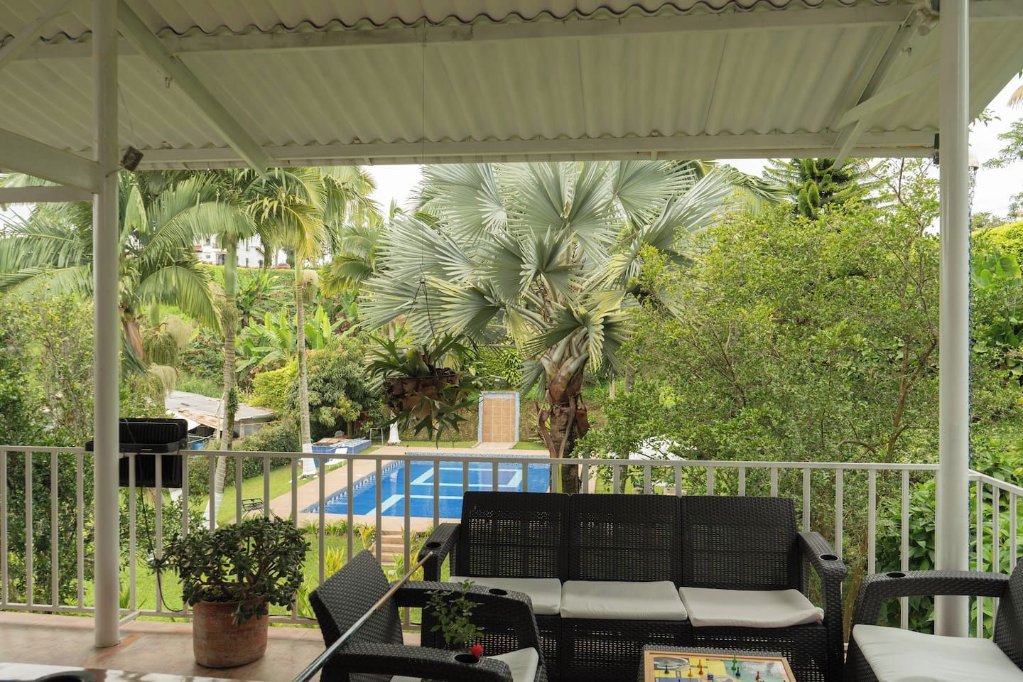 A covered outdoor seating area with a pool in the background.