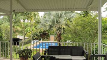 A covered outdoor seating area with a pool in the background.