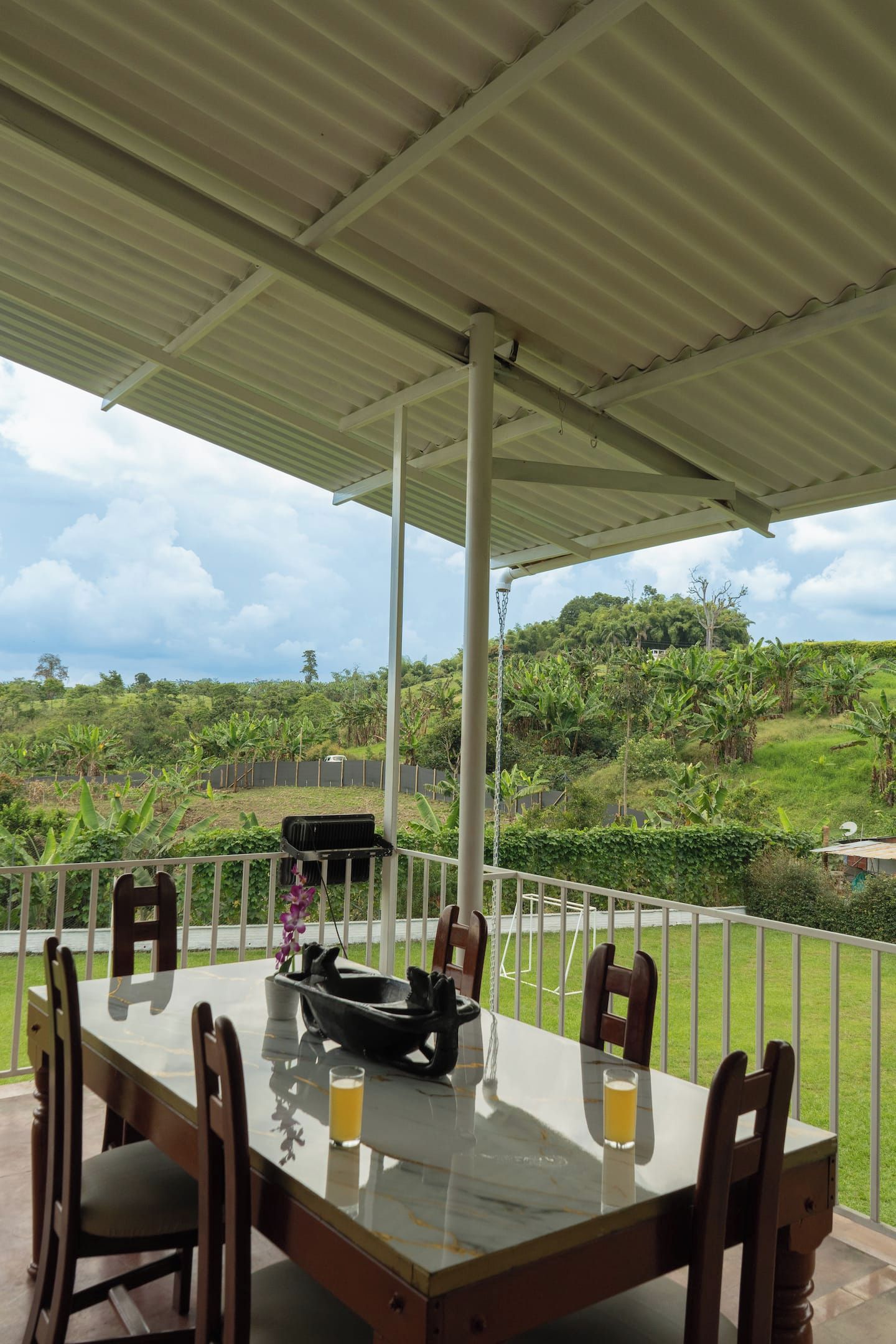 An outdoor dining area with a table and chairs, a grill, and a view of a lush landscape.