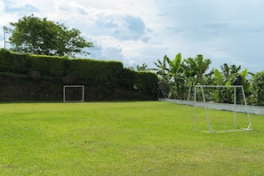 A grassy field with a soccer goal and a swing set.