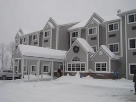 Un edificio de varios pisos con un porche cubierto y un techo cubierto de nieve.