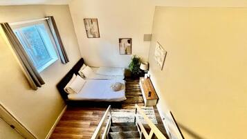 A bedroom with a bed, a window, a staircase, and a plant.