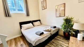 A hotel room with a double bed, a potted plant, a lamp, and artwork on the walls.