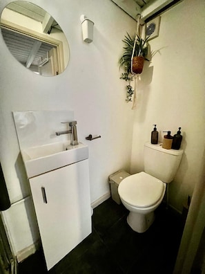 A compact bathroom with a white sink, a toilet, and a mirror. - Apartment Sleeps 4 Near Station (Purley)