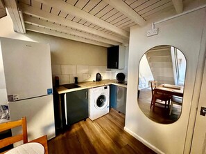 A compact kitchen with a washing machine, a dining area with a table and chairs, and a large mirror reflecting the room. - Apartment Sleeps 4 Near Station (Purley)