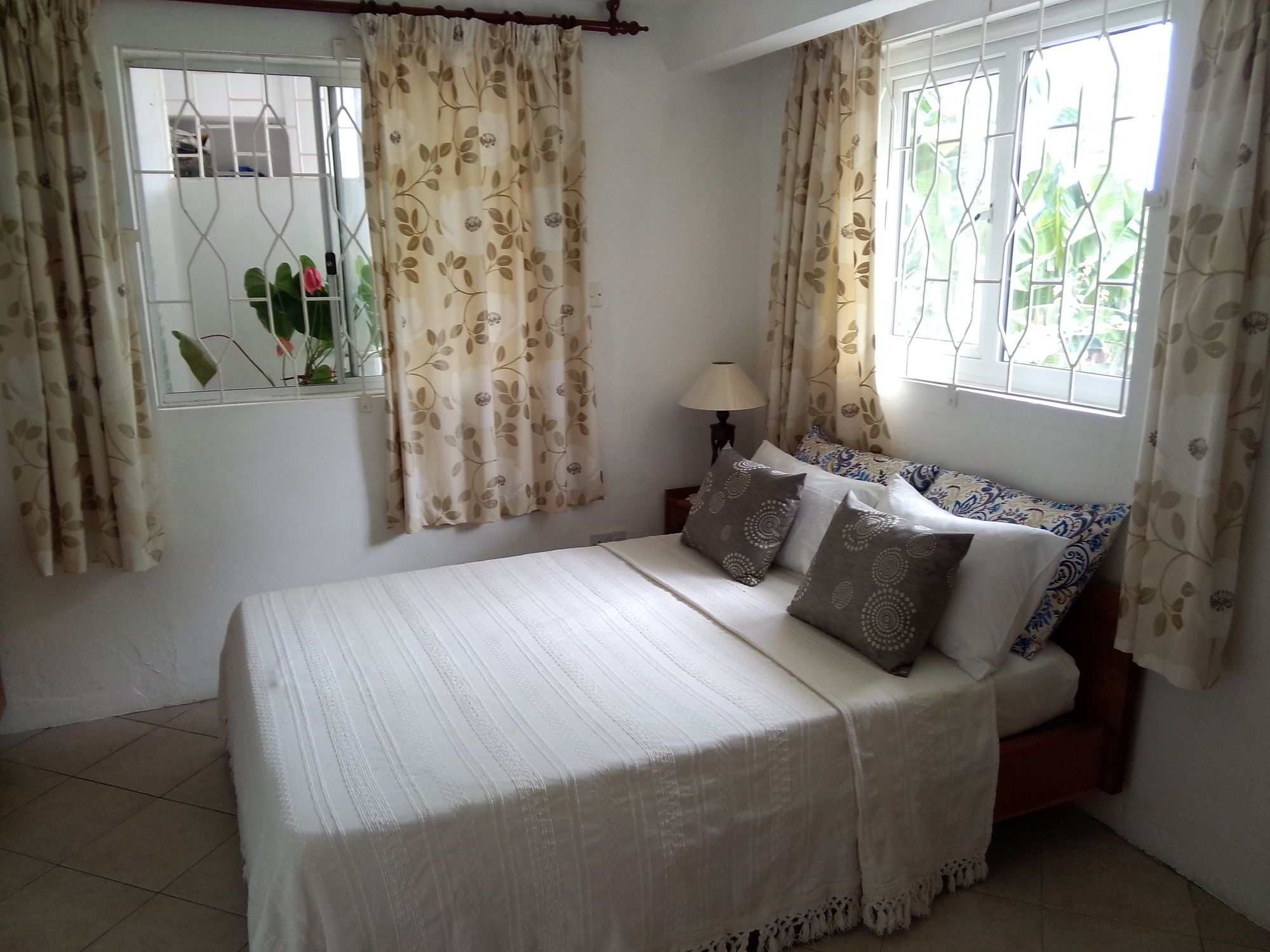 Un dormitorio con cama, cortinas, una ventana y una lámpara de noche.
