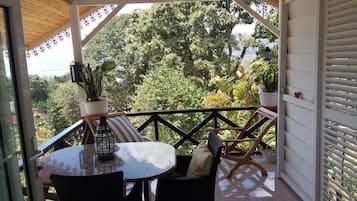 Un espacio de estar al aire libre cubierto con una mesa y sillas, rodeado por una barandilla de madera y plantas en macetas.