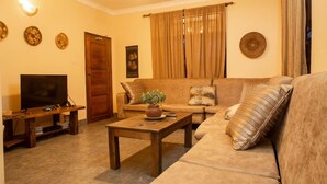 A living room with a sofa, a coffee table, a television, and decorative wall art. - White House of Tanzania - Hostel (Arusha)