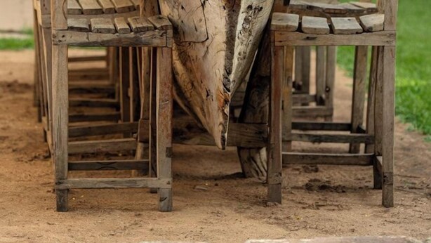 A rustic outdoor dining area with a long wooden table and chairs, surrounded by a wooden pergola. - White House of Tanzania - Hostel (Arusha)