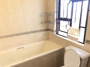 Un baño con bañera, inodoro y ventana, con una toalla colgada.