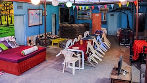 A dining area with a long table and chairs, a sofa with a red and black checkered cover, and a mural on the wall. - White House of Tanzania - Hostel (Arusha)