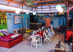 Un comedor con una mesa larga y sillas, un sofá con funda a cuadros rojo y negro, y un mural en la pared.