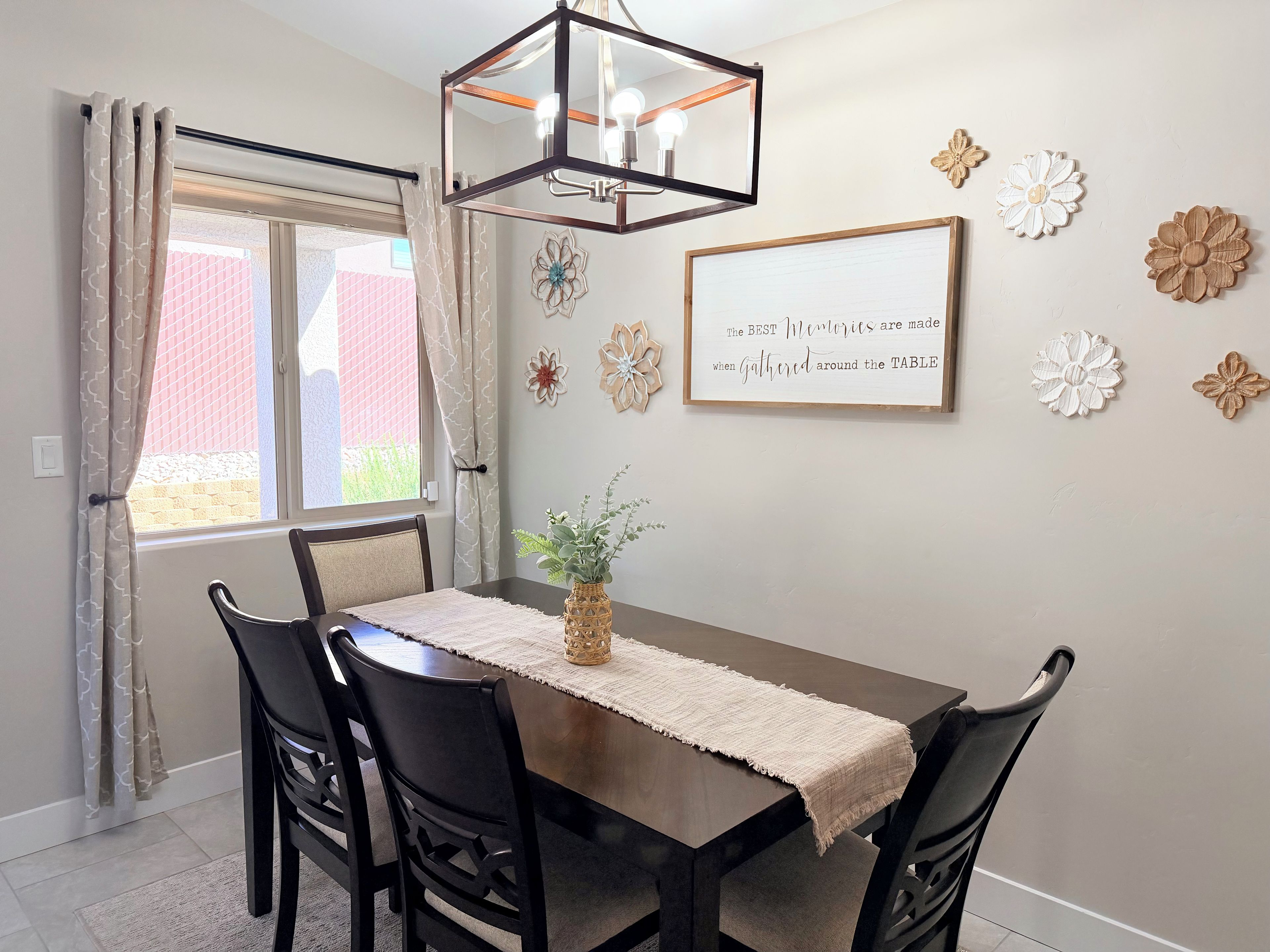 Un coin repas avec une table en bois, des chaises noires, un set de table en fibres naturelles, un luminaire suspendu et des œuvres d’art décoratives accrochées au mur.