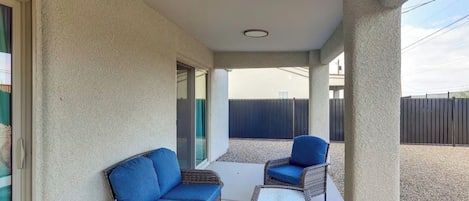 Un porche cubierto con muebles de mimbre y un ventanal que da a un espacio exterior.