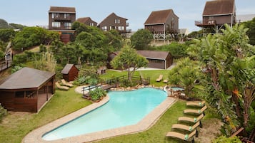 A pool area with lounge chairs, a wooden deck, and a view of multiple wooden buildings.