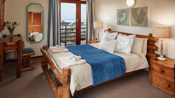 A hotel room with a wooden bed, a wooden nightstand, a mirror, and a view of the sea.