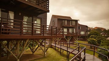 A wooden structure with multiple levels, including a deck and balconies, surrounded by greenery.