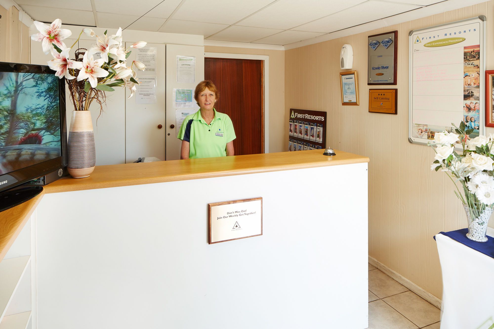 A reception desk with a sign that reads 'Don't Miss Out! Join Our Weekly Get Together!' in a hotel lobby.