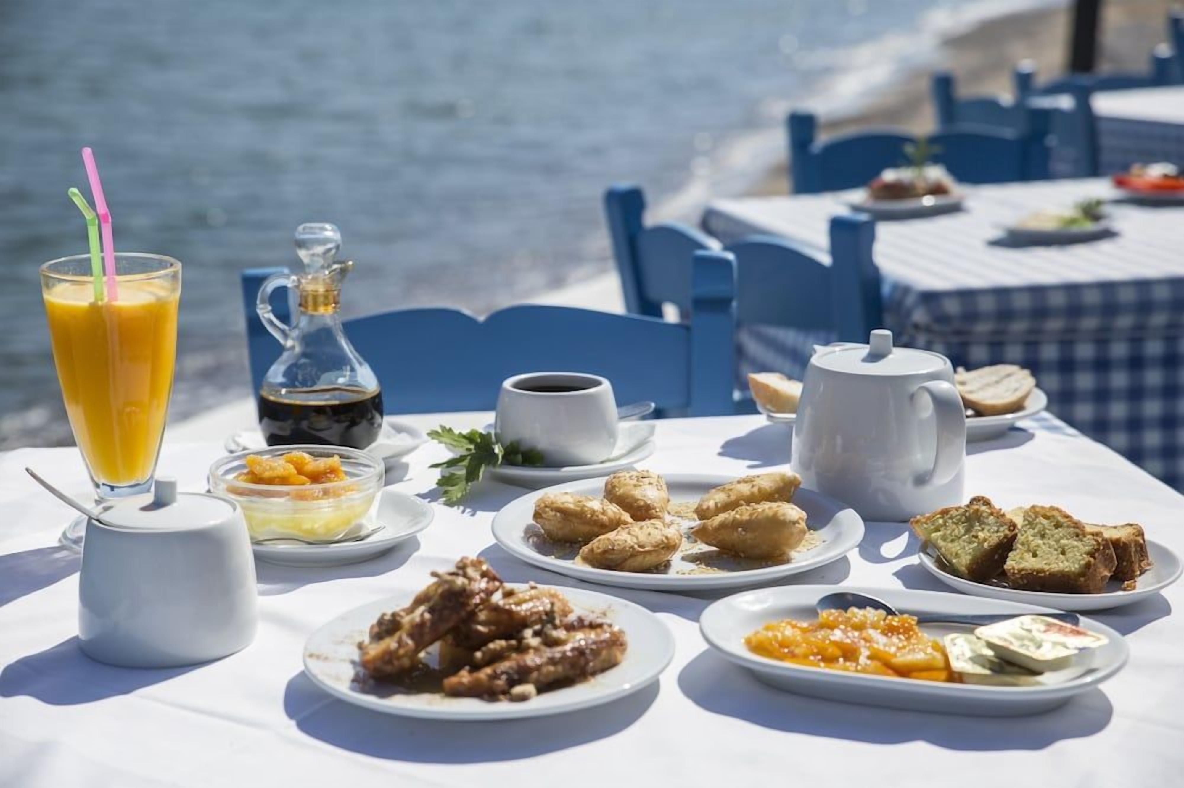 Une table dressée pour le petit-déjeuner, avec des œufs, des toasts et du jus, et une vue sur la mer en arrière-plan.