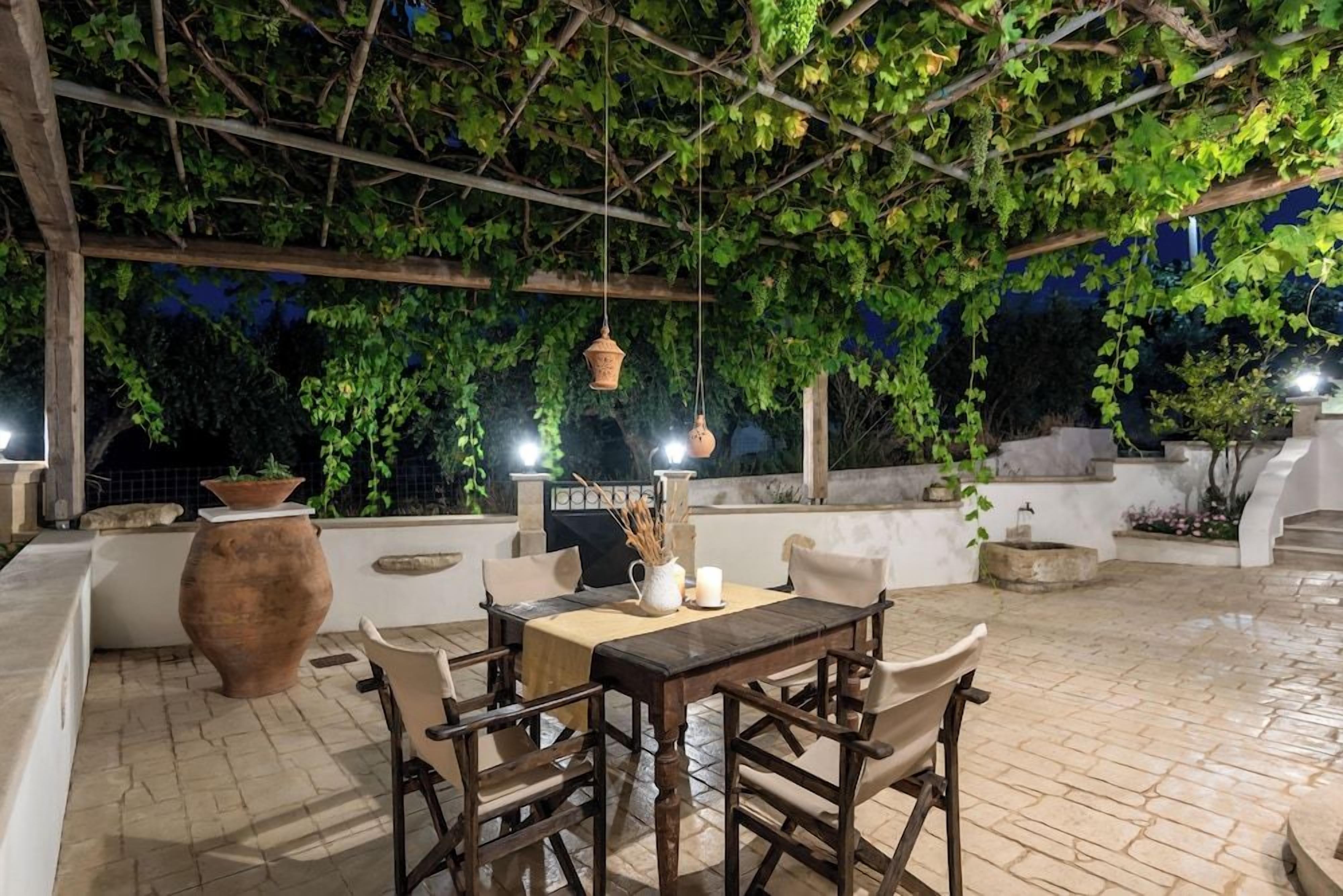 Um pátio externo com mesa e cadeiras, cercado por vegetação e piso de pedra.