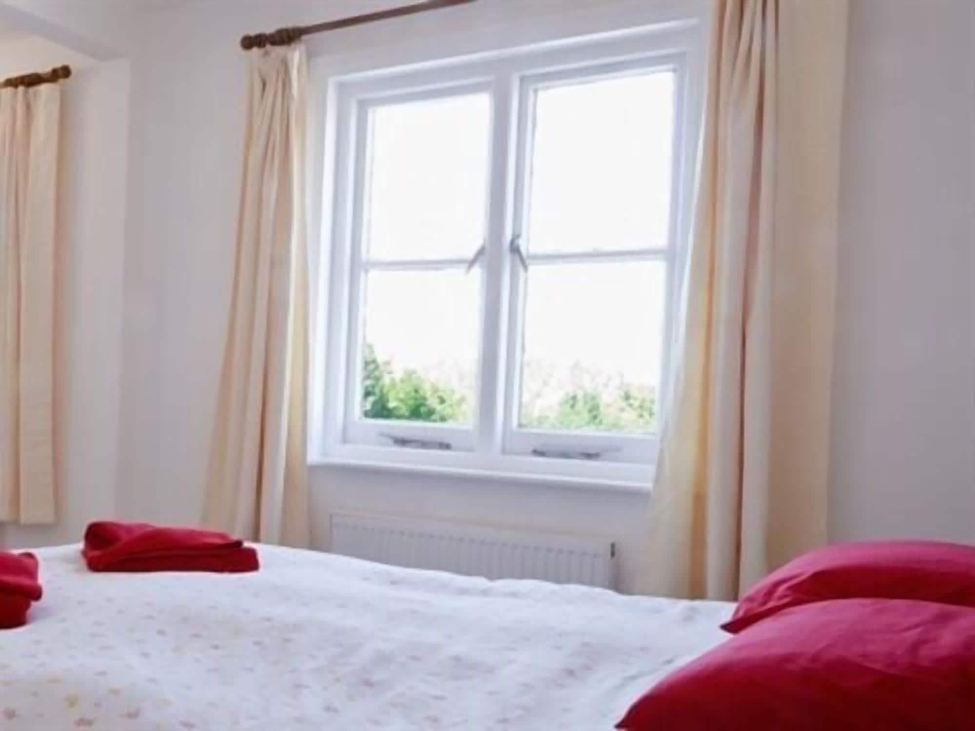 A bedroom with a large window, a bed with red pillows, and a radiator below the window.