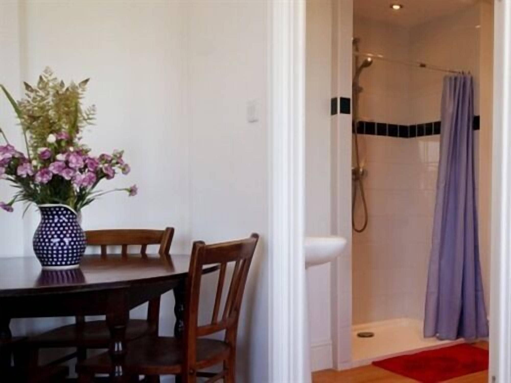 A room with a dining table, chairs, a vase with flowers, and a shower area with a curtain.