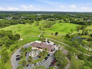Un parcours de golf doté d’un club-house, d’un parking et entouré de verdure.